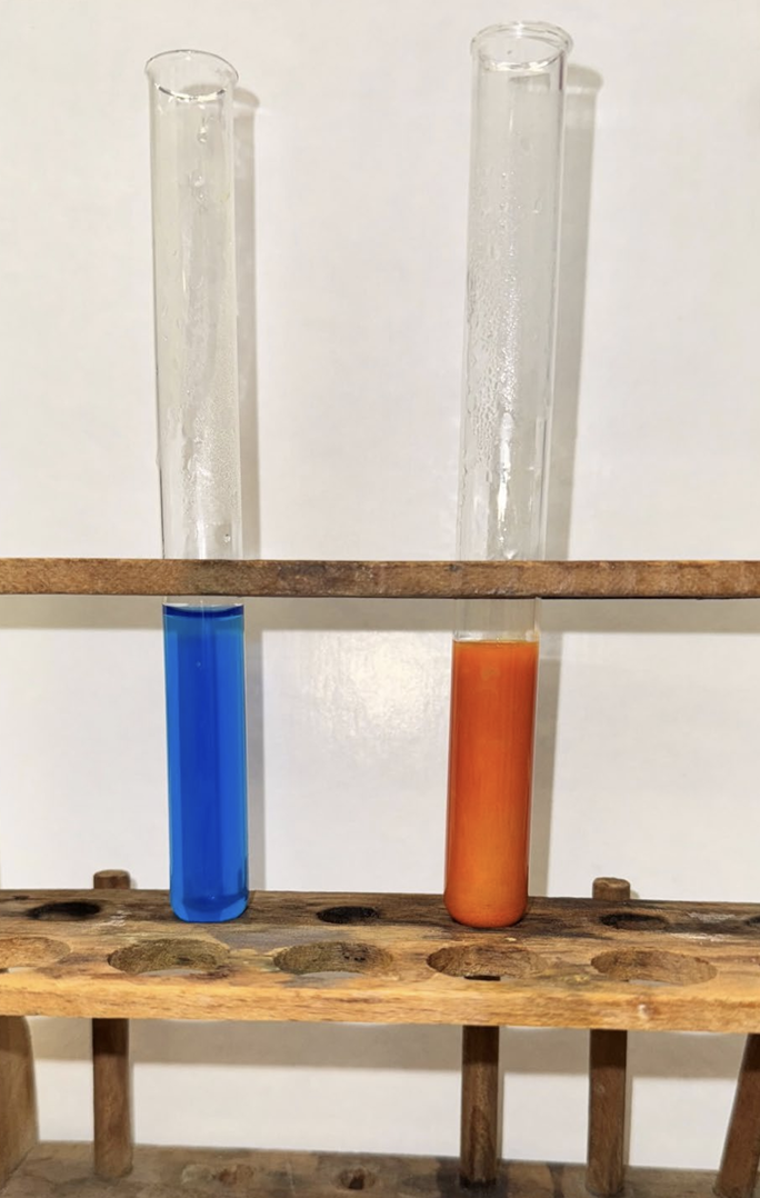 Zwei Reagenzgläser in Holzgestell mit blauer und oranger Flüssigkeit.